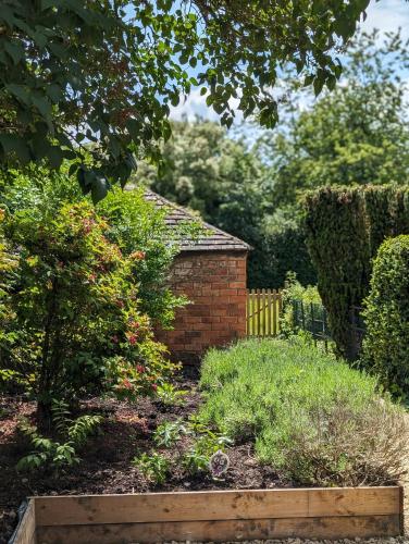 a garden with a brick building and some bushes at School View Cottage in North Cerney