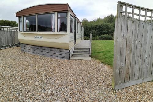 a tiny house sitting on top of gravel next to a fence at 3 Bedroom Caravan in Rural area - Tennyson in Porchfield