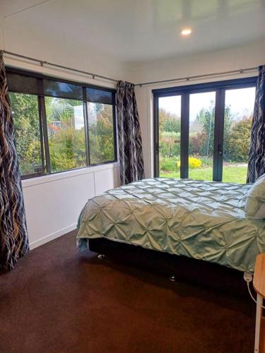 a bedroom with a bed and two large windows at The Guest House in Tamahere