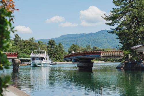 un barco que viaja por un río con un puente en 珀 Haku, en Miyazu