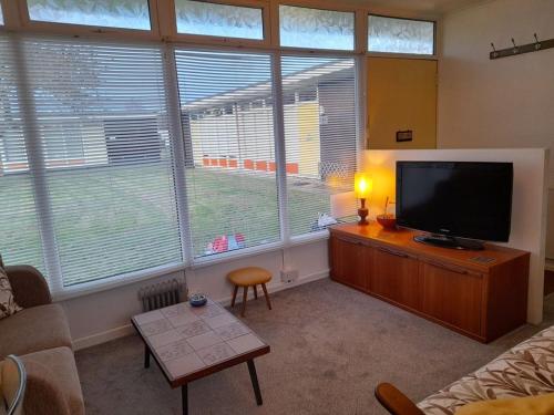 a living room with a flat screen tv and large windows at Retro Inspired Holiday Home in the Norfolk Broads in Stalham