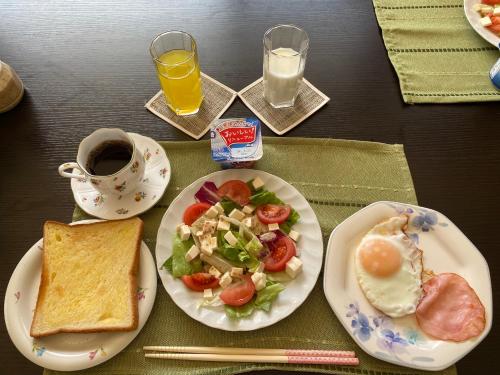 a table with plates of food and a cup of orange juice at Kei Chia Private Lodging in Kurihashi