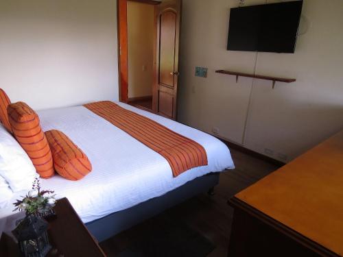 a bedroom with a bed with orange pillows and a television at Chalet Campestre la Peseta in Ubaté