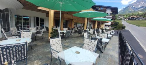 a patio with tables and chairs with green umbrellas at Wellness & Sporthotel Alpenhof in Ehrwald