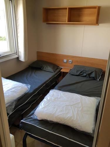two beds in a small room with a window at Mobil home Aventura 8 places in Gastes