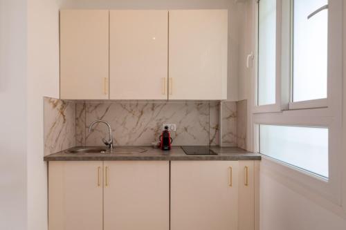 une cuisine avec des armoires blanches, un évier et une fenêtre dans l'établissement Beau Studio Le Grand Palais 100m des plages, à Juan-les-Pins