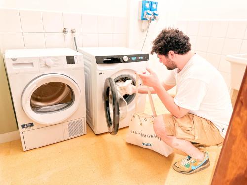 a man sitting on the floor next to a washing machine at Ostello Bello Palermo in Palermo