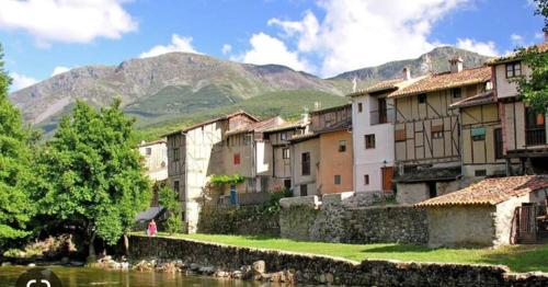 eine Gruppe von Gebäuden neben einem Fluss mit Bergen in der Unterkunft Aires Del Ambroz in Casas del Monte