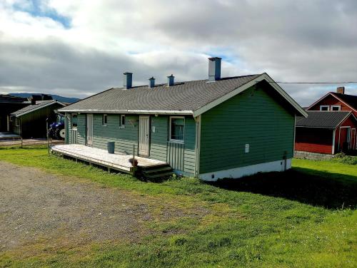 a green house with a porch on a field at Kongsfjord Holiday Home in Kongsfjord