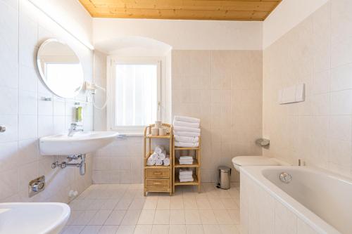 a white bathroom with a sink and a tub and a toilet at Central Apartments Cristlpek in Ortisei
