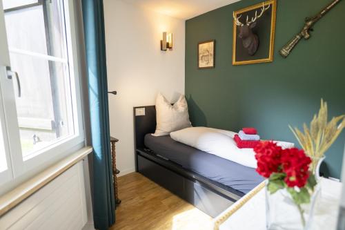 a small room with a bed with a vase of red flowers at Chasa Valbernard in Vulpera