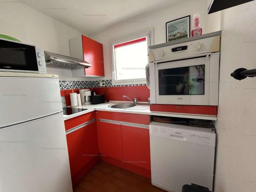 La cuisine est équipée de placards rouges et d'une cuisinière blanche. dans l'établissement Appartement rénové 2 pièces, 4 pers, à 150m de la mer - FR-1-229B-98, à Narbonne