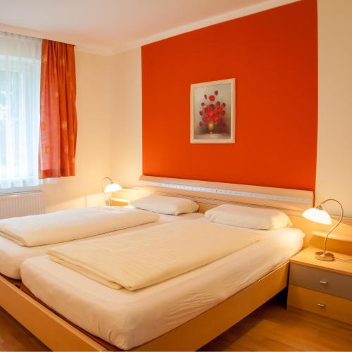 two beds in a room with an orange wall at Waldpension Schiefling am See in Schiefling am See