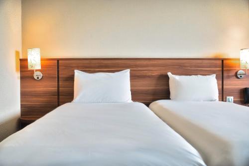 two beds in a hotel room with white sheets at Kyriad Prestige Mulhouse - Basel in Sausheim