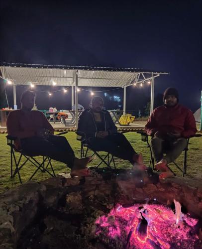 three men sitting around a fire at night at Kunjapuri camps & Cottage in Narendranagar