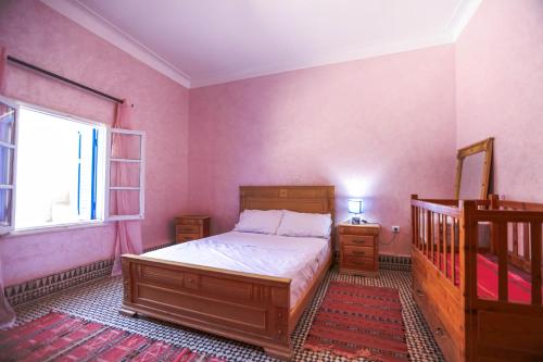 a bedroom with pink walls and a bed and a window at Riad Isla in Essaouira