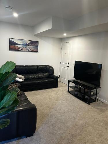 a living room with a black couch and a flat screen tv at Praise bethel -Homely walkout legal basement in YYC in Calgary