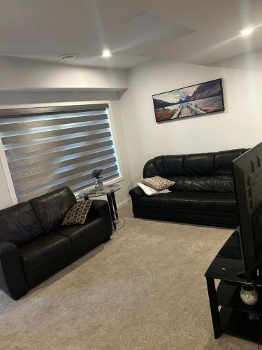 a living room with two black leather couches and a television at Praise bethel -Homely walkout legal basement in YYC in Calgary