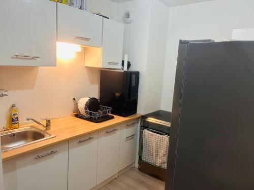 La cuisine est équipée d'un réfrigérateur noir et d'un évier. dans l'établissement Appartement 2 chambres meublé, à Corbeil-Essonnes