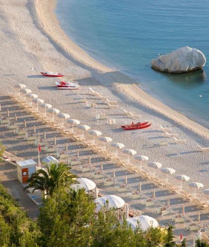 a beach with white umbrellas and chairs and the water at Murè Hotel Numana in Numana