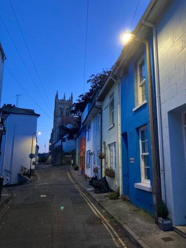 an empty street with blue houses and a church at Fisherman's Cottage - Harbour Close, Pub Closer, Sea Views if You Look Hard in Brixham