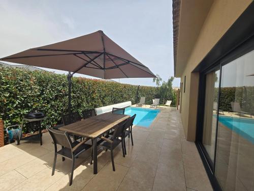 - une table et des chaises en bois avec un parasol à côté de la piscine dans l'établissement Résidence Villas Chléa, à Lucciana
