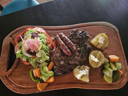 a wooden plate of food with meat and a salad at The Landing Hotel And Restaurant in Moyogalpa