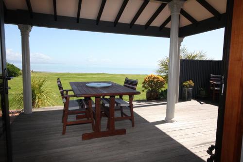 una mesa de madera y sillas en un porche con vistas al océano en Te Puru Beach Lodge en Te Puru