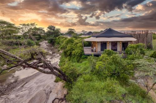 a house on the side of a river at JW Marriott Masai Mara Lodge in Masai Mara