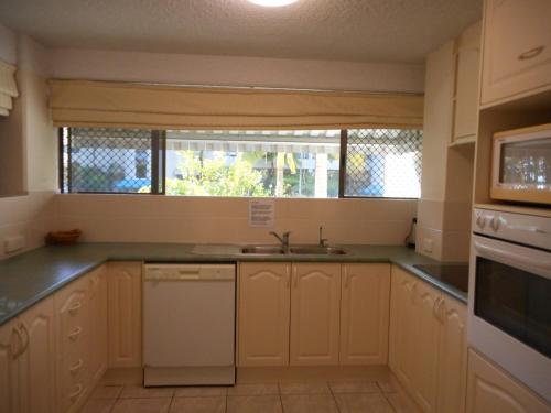 a kitchen with white cabinets and a sink and a window at Placid Waters Holiday Apartments in Bongaree