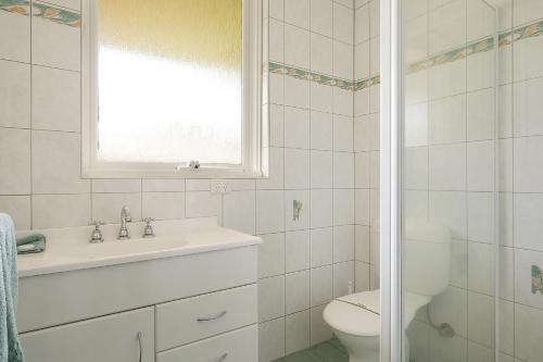 a bathroom with a sink and a toilet and a window at Kalindo Merimbula in Merimbula