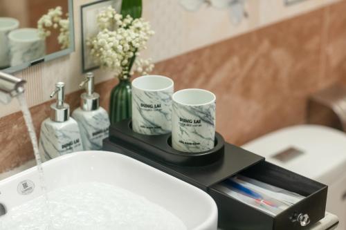 een badkamer met een wastafel en twee kopjes op een aanrecht bij DUNG LAI HOTEL 173 in Cat Ba