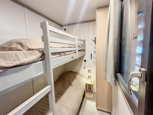 Cette petite chambre comprend des lits superposés et une fenêtre. dans l'établissement Chalet de Standing à Jullouville: 6 Couchages, Piscine Chauffée, Proche Plage et Commerces, WiFi Gratuit - FR-1-361-548, à Jullouville