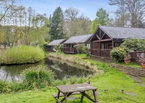 a house with a picnic table next to a river at Tilford Woods Lodge Retreat in Farnham