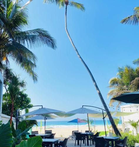 a beach with tables and umbrellas and palm trees at Josan Villa with a Glorious Beach and Sea View in Habaraduwa