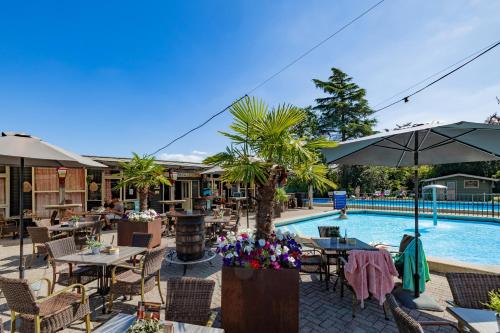 an outdoor patio with tables and umbrellas next to a pool at Woodlodge de luxe 2 persoons in Oorsbeek