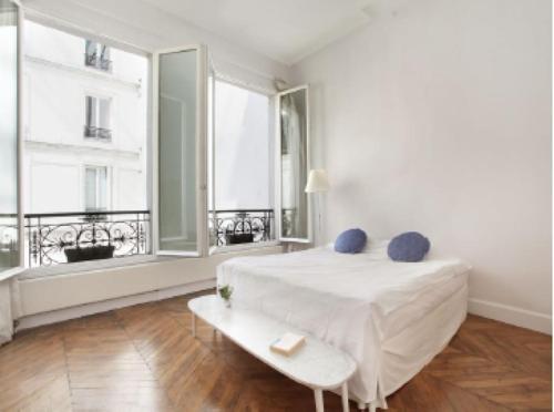 une chambre blanche avec un lit et deux fenêtres dans l'établissement appartment d'architecte, à Paris