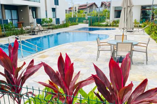 a resort pool with tables and chairs and plants at Studio de Luxo em Muro Alto - Makia Beach A209 in Porto De Galinhas