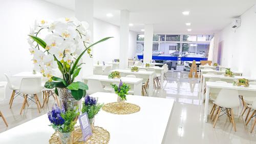een restaurant met witte tafels en witte stoelen en bloemen bij Pousada da Bia Praia in Penha