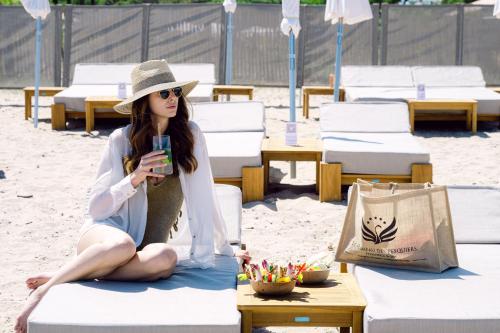 a woman sitting on the beach holding a drink at Le Hameau Des Pesquiers Ecolodge & Spa, Curio Collection By Hilton in Hyères