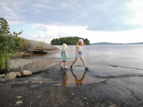 a woman and a child walking on the shore of a body of water at Kelo Villa for 8, with hot tub, by lake Päijänne in Jyväskylä