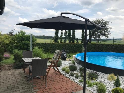 a patio with a table and an umbrella next to a pool at Příjemný apartmán Křoví v rodinném domku se sdíleným bazénem, terasou a zahradou in Křoví