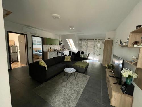 a living room with a black couch and a kitchen at Belle Apartman in Balatonlelle
