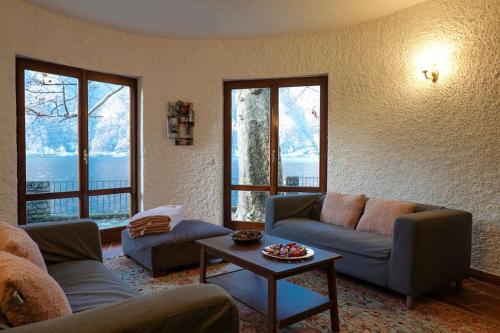 a living room with couches and a table and windows at Secluded Cottage front Lake with BOAT in Valsolda