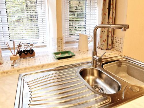 a stainless steel sink in a kitchen with windows at THE OLD WASH KITCHEN - Charming Character Cottage in Holmfirth, Yorkshire in Holmfirth