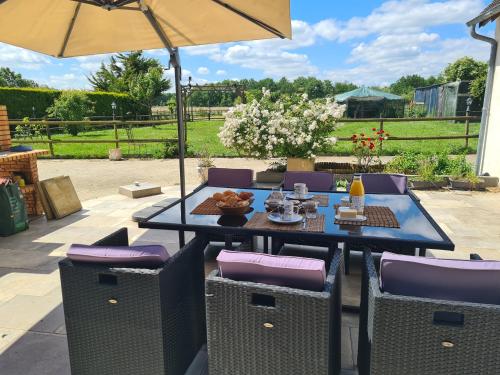Una mesa de comedor con sillas moradas y una sombrilla. en La villa des Roses - Chambre au calme et une chambre supplémentaire à partir de la 3ème personne, en Le Perray-en-Yvelines