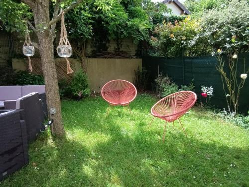 two red chairs sitting in the grass next to a tree at 2 chambres d'hôtes in Wissous