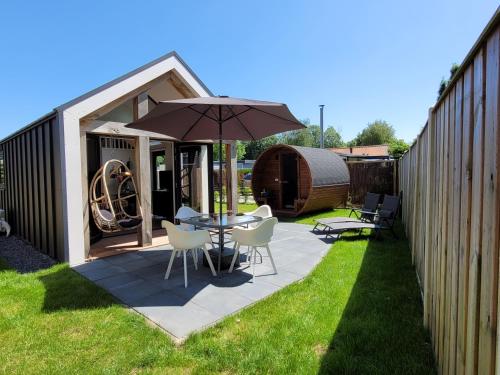 a patio with a table and chairs and an umbrella at Tiny Zen House in Heinkenszand with private sauna, airco, outdoor swimming pool, WiFi and 2 bedrooms in Heinkensand