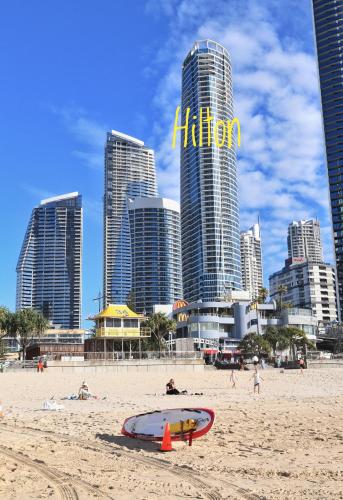 a beach with a surfboard on the sand with tall buildings at Spectacular 19th Floor Apartment in Heart of Surfers Paradise in Gold Coast