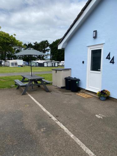 a picnic table with an umbrella next to a building at 44 Gower holiday village Ty Gŵyr Cosy 2 bedroom Chalet with a seasonal indoor pool in Swansea